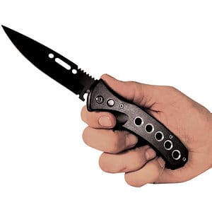 Hand holding a black folding knife with a sleek design and circular handle cutouts.