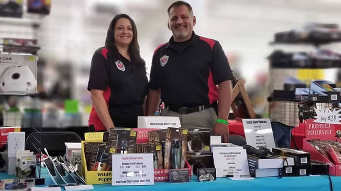 Two people at a pepper spray booth showcasing products at a market event.