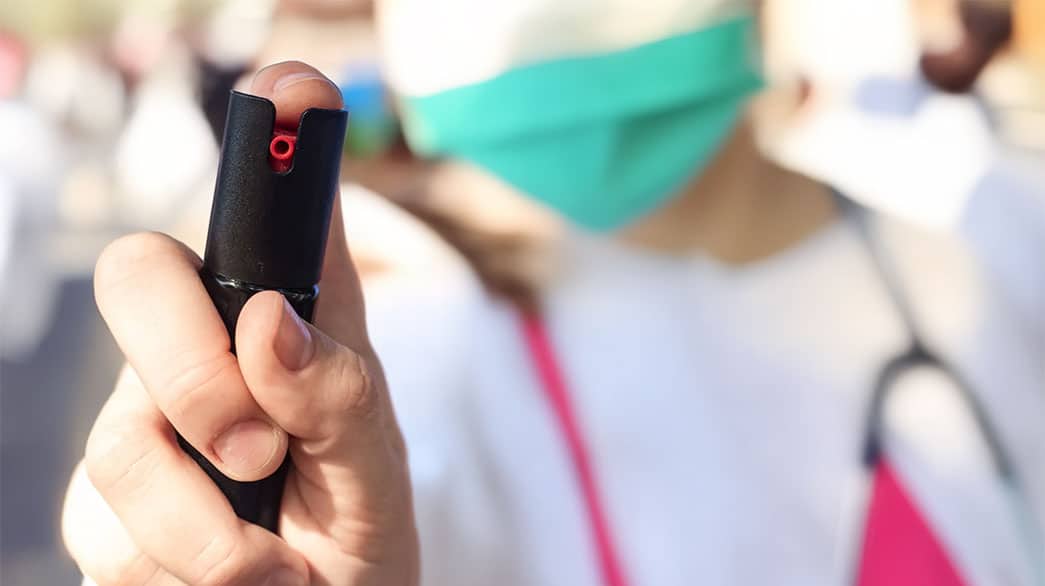 Person holding pepper spray for self-defense, wearing face mask, close-up view.