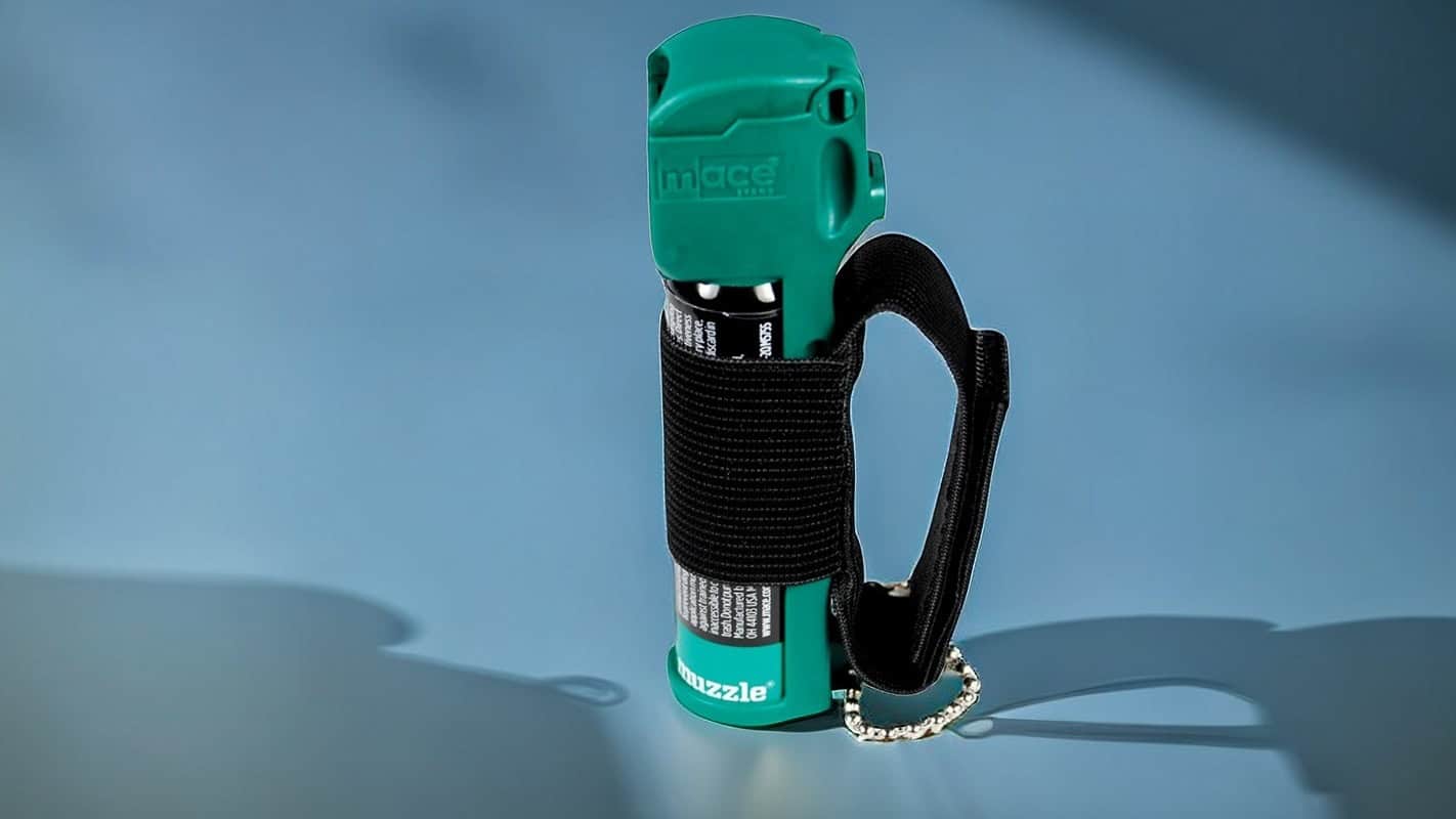 Green pepper spray can with black holster on blue background, personal safety accessory.