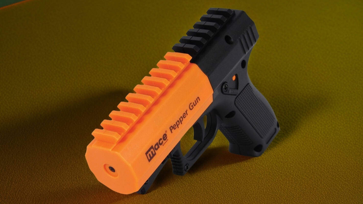 Orange and black Mace pepper spray gun on a green surface, showcasing personal safety device features.