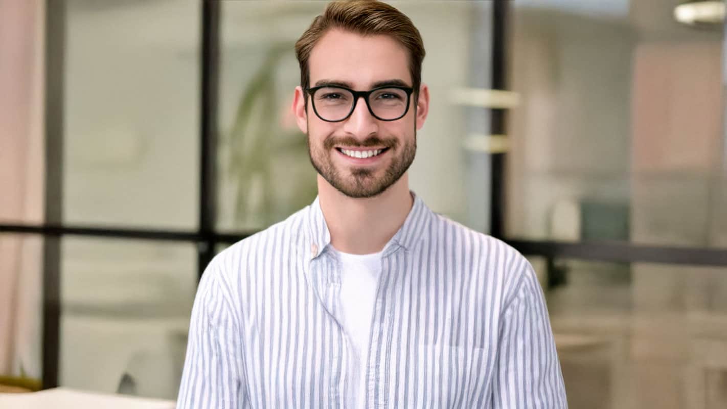 Smiling man in glasses and striped shirt in modern office setting.