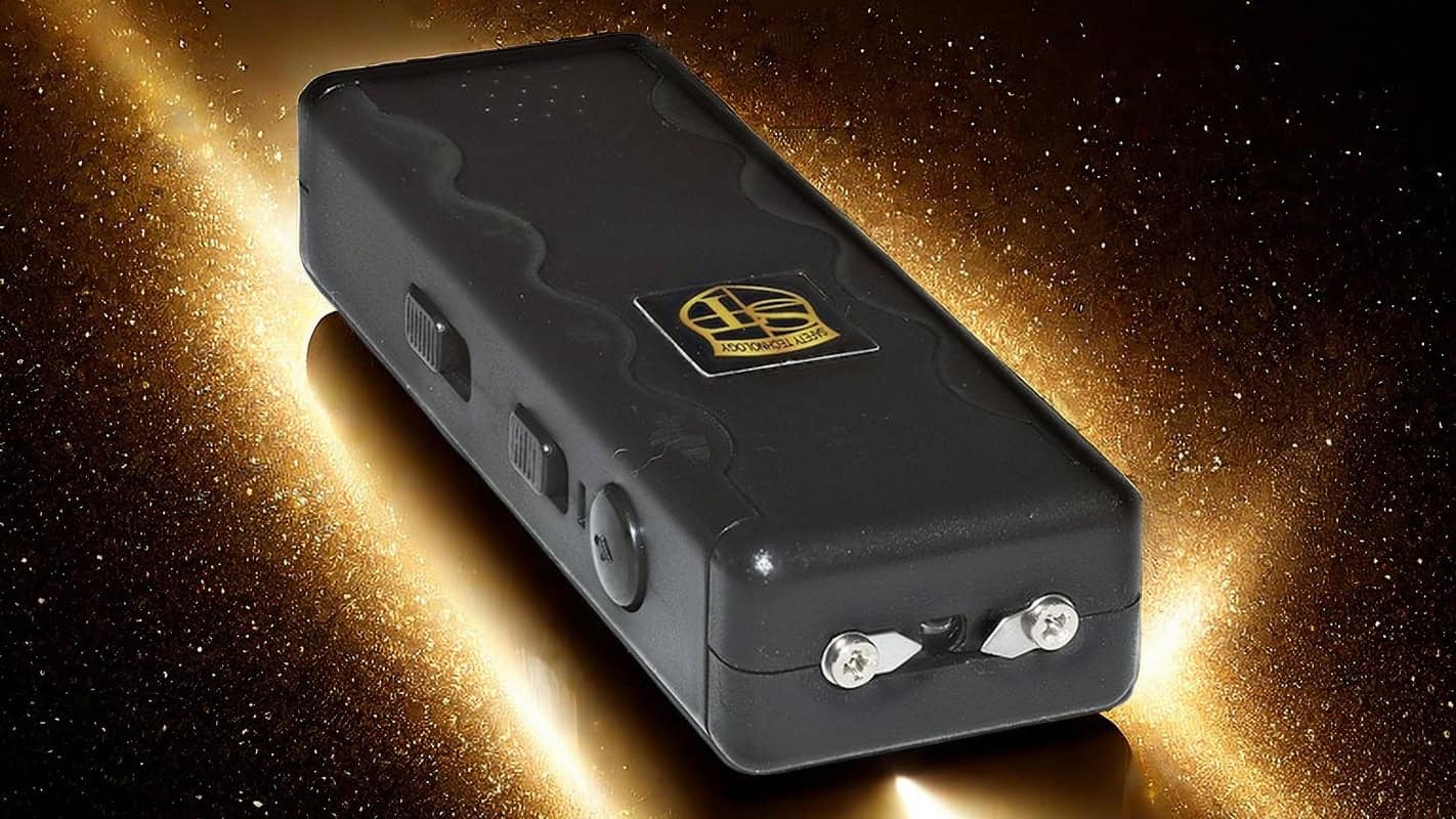 Black stun gun with gold background, featuring a textured grip and safety switch for personal security.