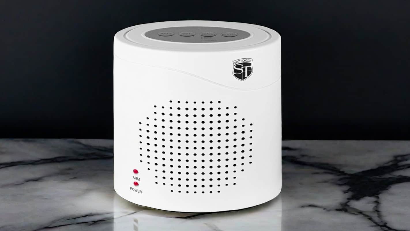 White portable speaker on a marble surface, featuring control buttons and a branded logo.