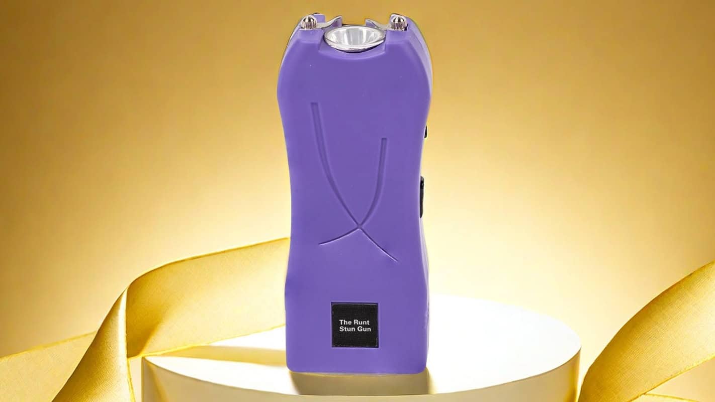 Purple stun gun on a white platform with a yellow background, showcasing the compact design and safety features.